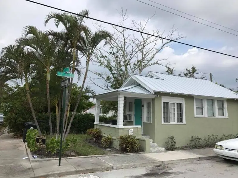 Green bungalow with a silver metal roof and a white porch