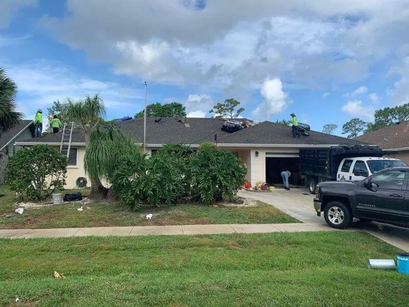 Crew installing new dark asphalt shingles on a single-story home