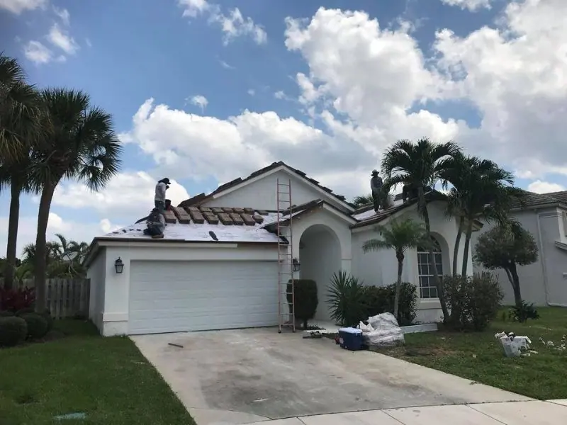 Crew setting concrete roof tile on a white stucco home with palm trees