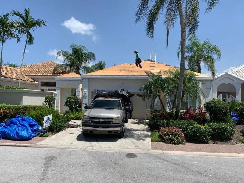 Roofer on a tile re-roof with fresh orange underlayment and the crew truck below
