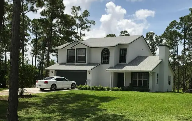 Two-story white home with a new gray shingle roof among tall pines